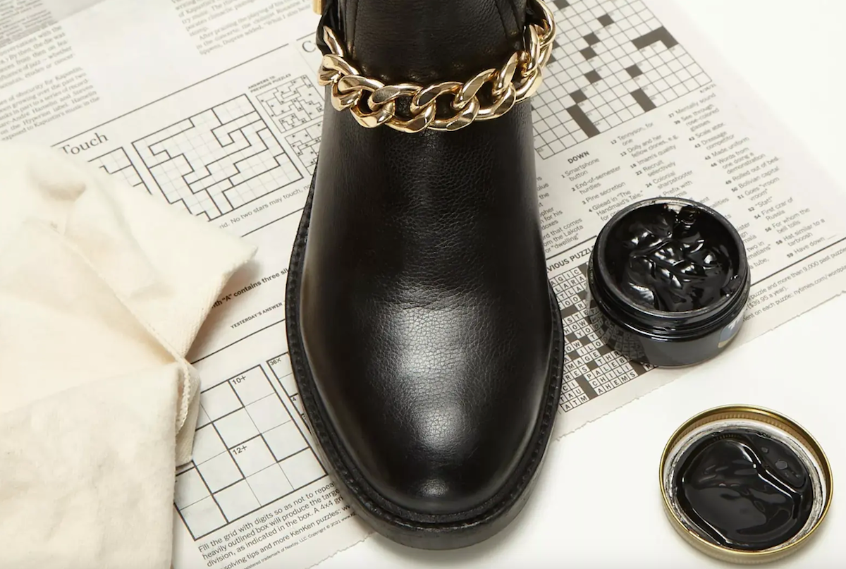 A birds-eye shot of a black leather booto with cleaning supplies, including shoe polish and a brush.