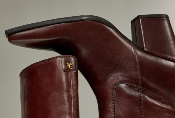 Close-up of brown leather Vince Camuto knee-high boots with block heels and gold VC logo.