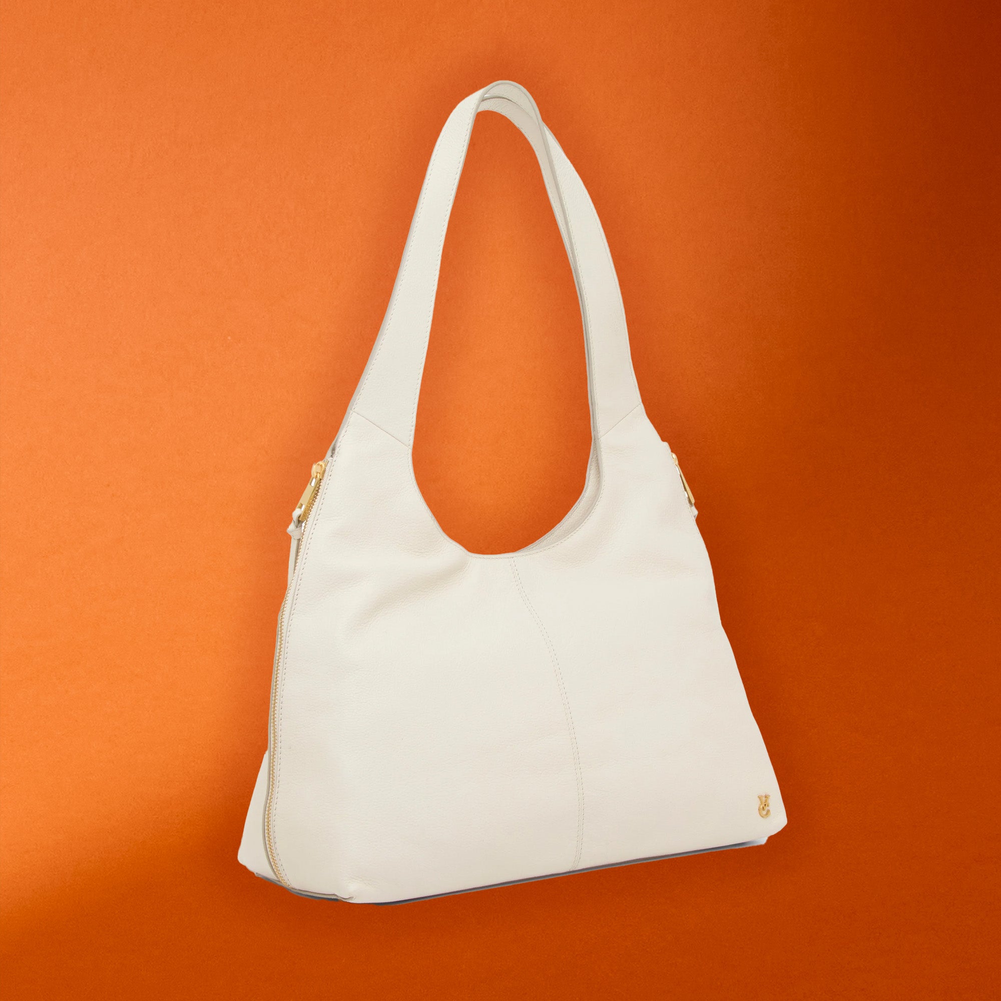An off-white leather shoulder bag with gold-tone hardware, shown against a solid orange background.