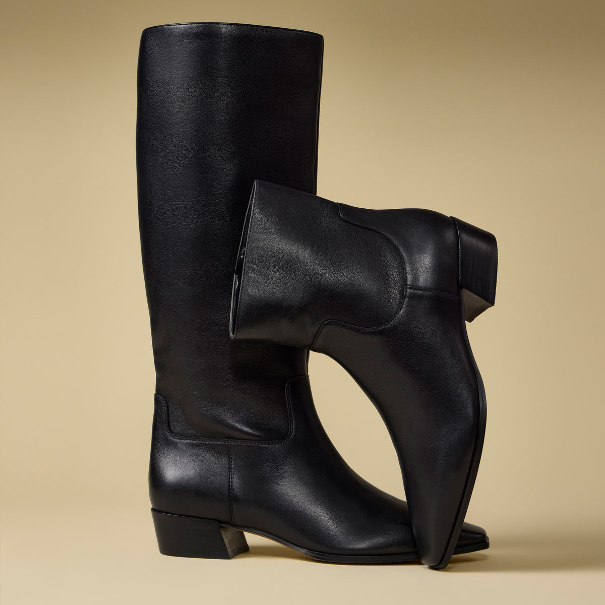 1 tall boot and one black bootie against a tan backgroud