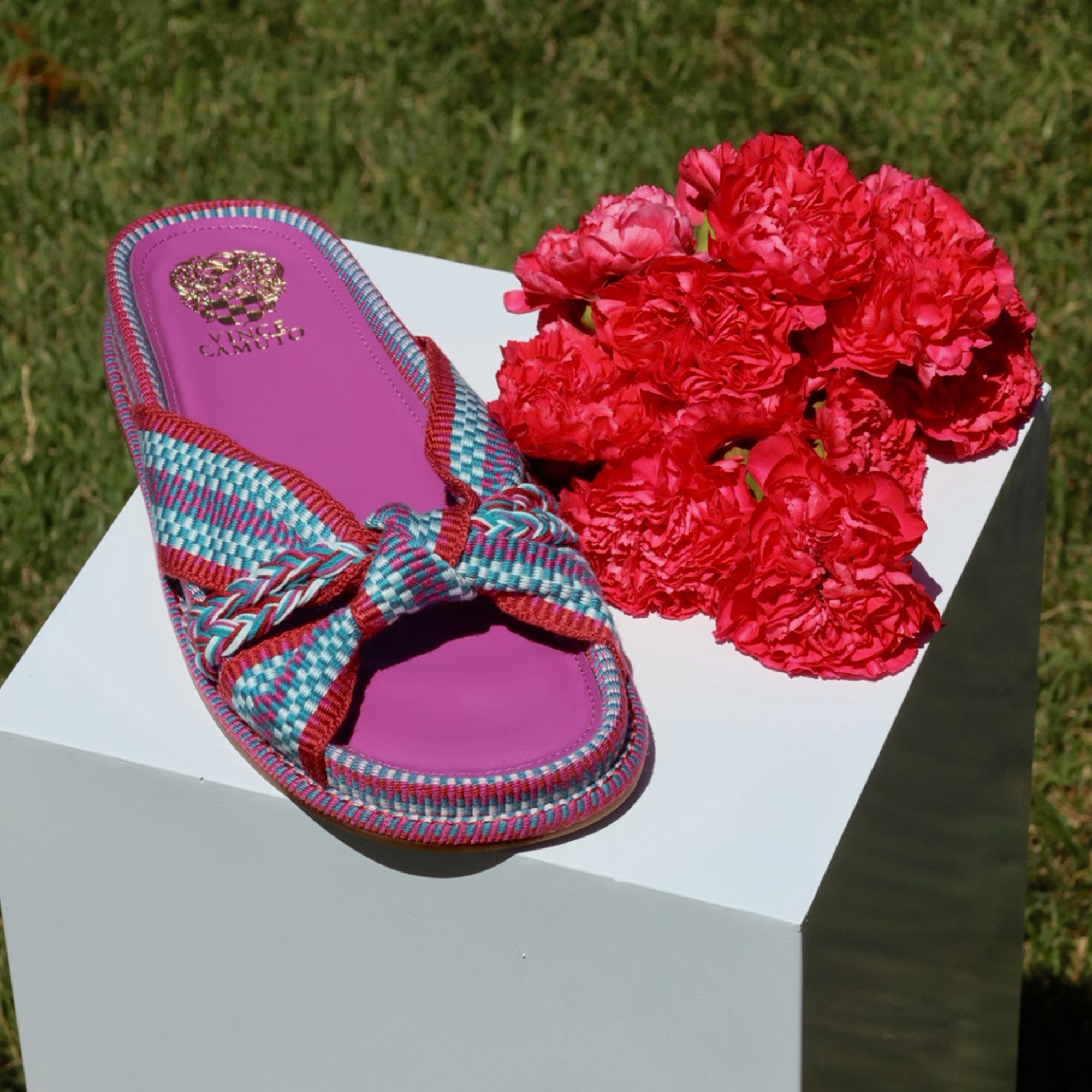Colorful sandal with pink sole on a white surface next to red flowers outdoors.