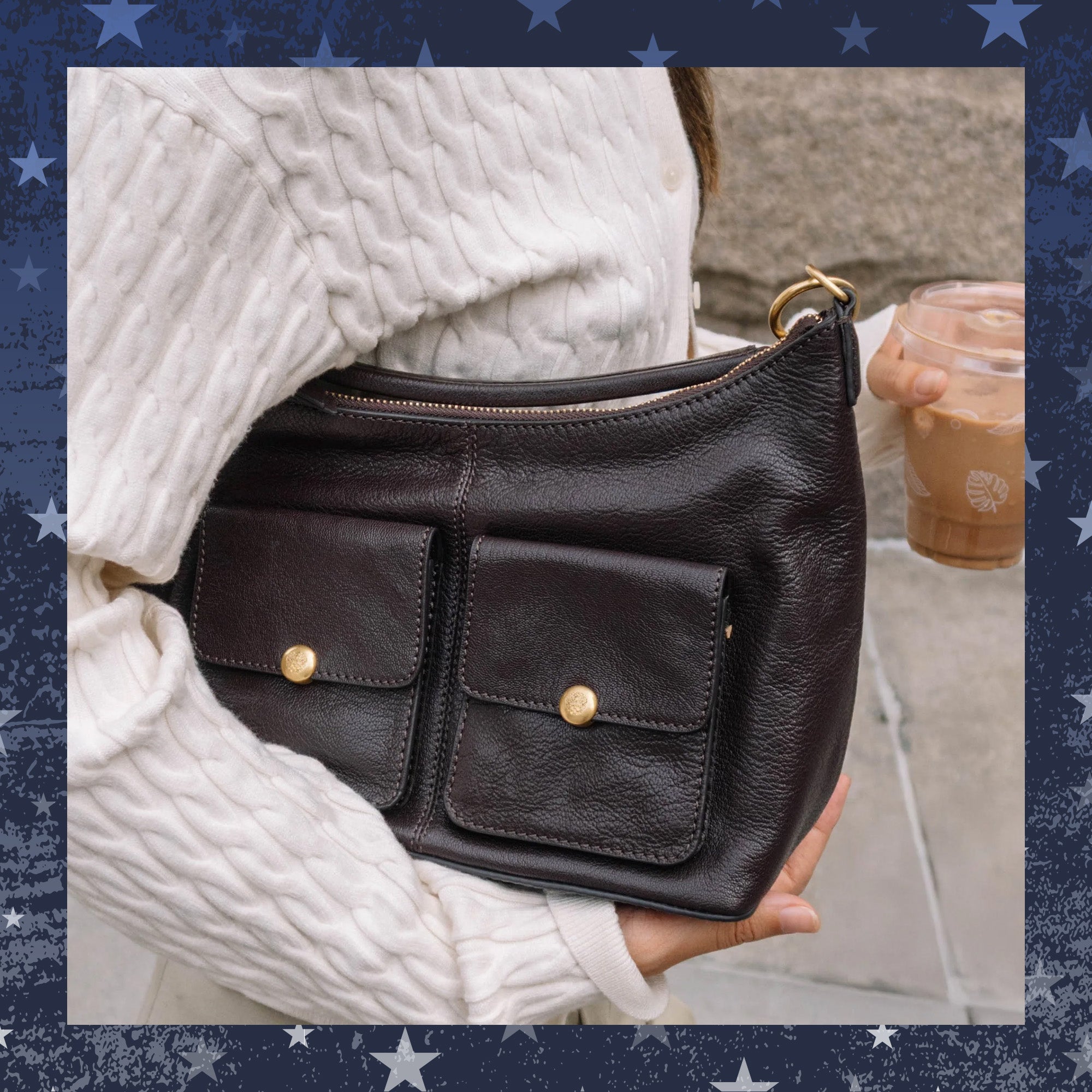 Black leather handbag held by a person wearing a white sweater, with a blurred background.