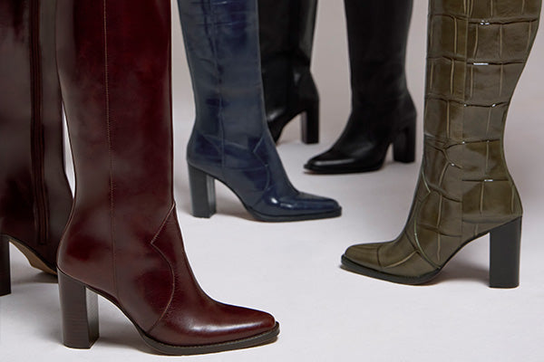 A group of high-heeled knee-high boots in different colors, including burgundy, navy blue, black, and olive green, arranged on a light studio background.