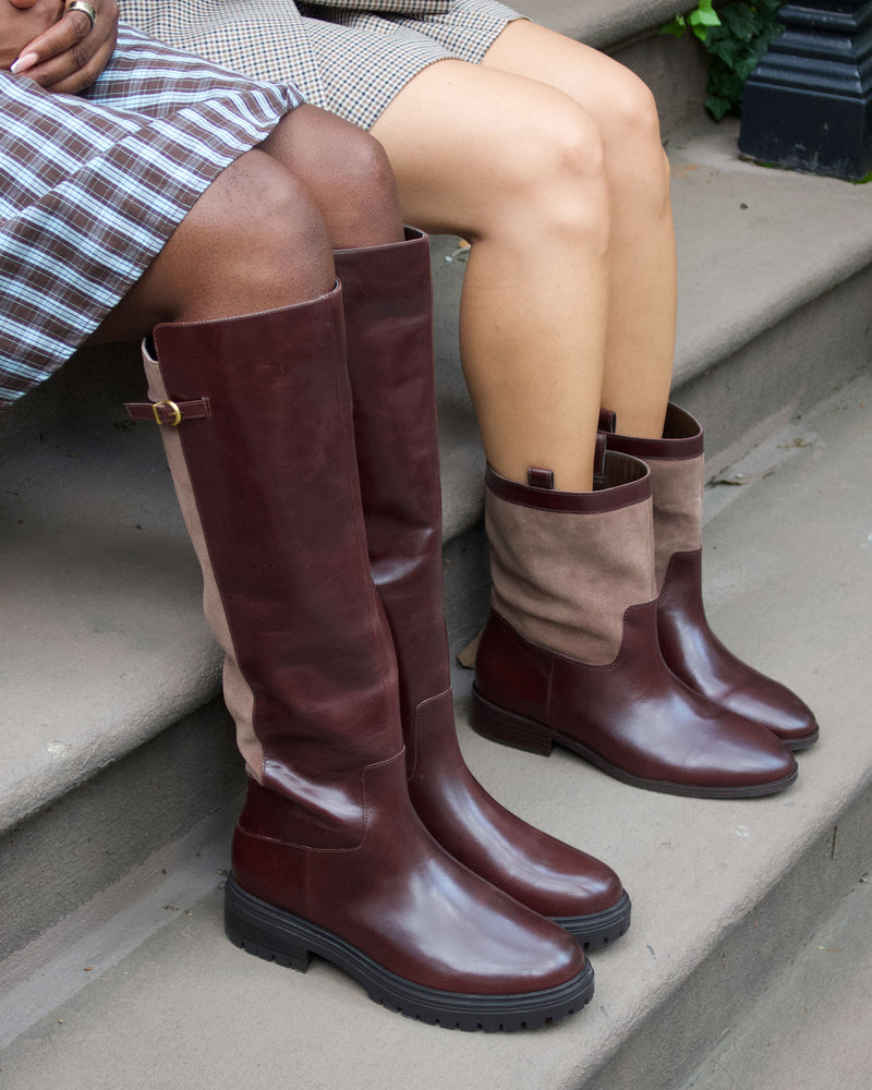 Two people sit on stone steps, their legs visible as each wears a plaid skirt or dress paired with stylish Vince Camuto Bertla Wide Calf Knee High Riding Boots in rich burgundy leather with brown suede panels.
