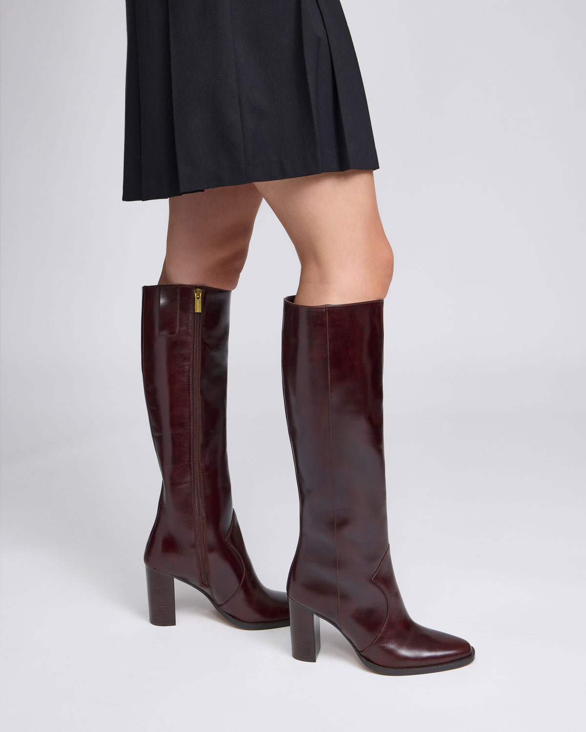Person wearing dark maroon Vince Camuto Lecheya Narrow Calf Knee High Boot knee-high block heel boots with side zippers.