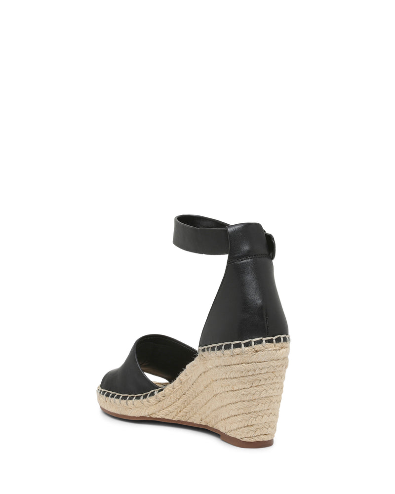 The Vince Camuto Leera Espadrille Wedge Sandal is shown from the back on a white background, featuring black leather, an ankle strap, and a woven espadrille platform heel.