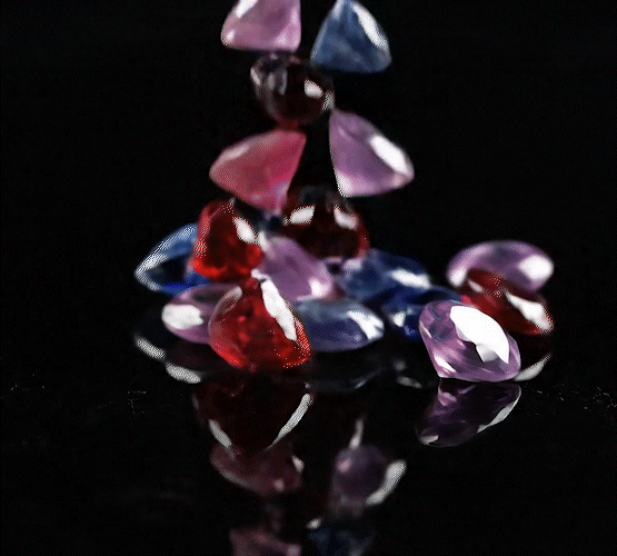 Video of multi-colored jewels slowly falling onto a mirrored surface
