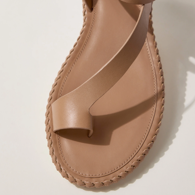Close-up of a tan leather sandal featuring a wide strap across the foot and a loop for the big toe, with detailed stitching along the sole’s edge.