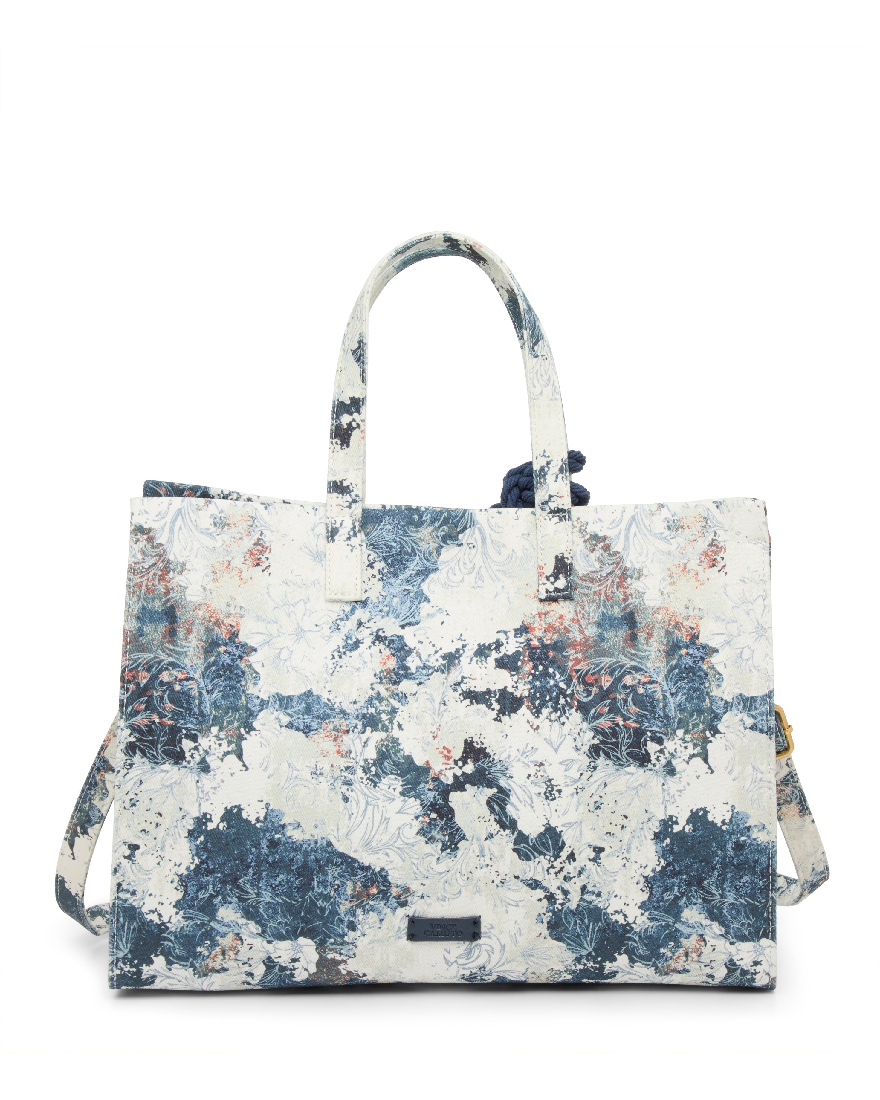 The Vince Camuto Aalis Tote Bag is a rectangular canvas handbag with short handles and a shoulder strap, featuring a blue, white, and beige abstract floral print and a metallic logo plate on the front.