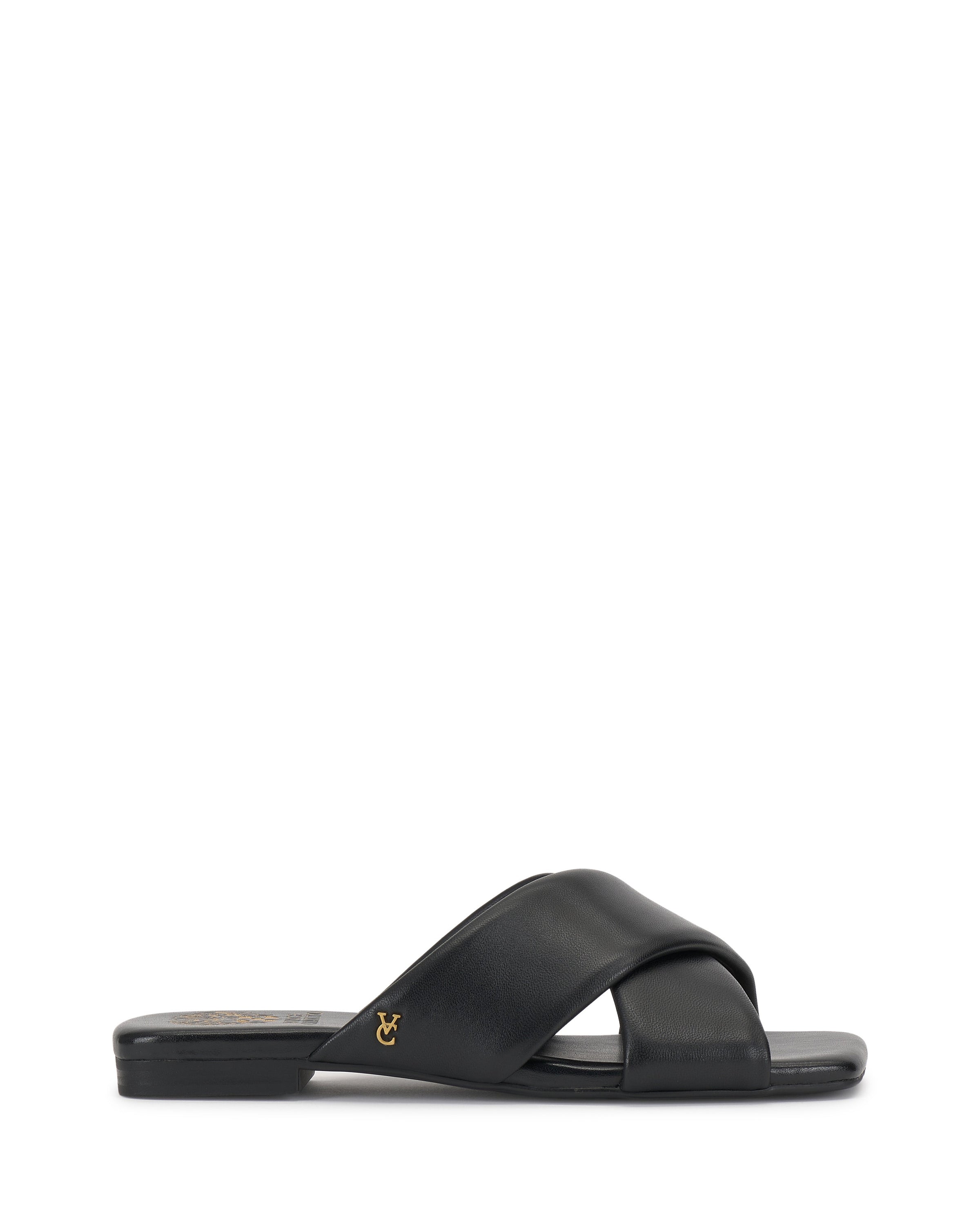 The Vince Camuto Adisey Cross-Band Sandal is a black flat slide with wide crisscross straps and a small gold logo on the side, ideal for daily wear. Shown in side profile on a white background.
