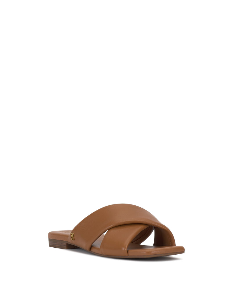 The Vince Camuto Adisey Cross-Band Sandal offers a comfortable fit with wide crisscross straps and a small gold logo accent, ideal for everyday wear. Pictured in brown on a plain white background.