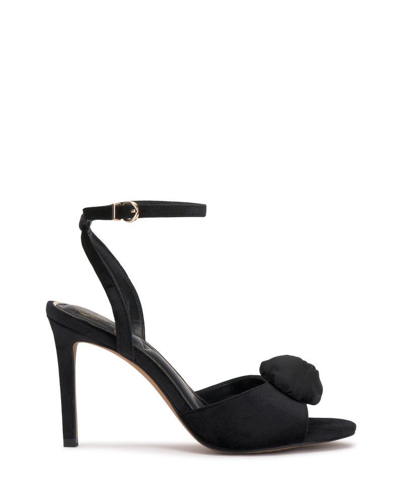 The Vince Camuto Aisven Sandal is a black high-heeled sandal featuring an ankle strap, open toe, and a decorative bow at the front. With its thin elegant heel and minimalist, sophisticated design, this shoe is the perfect blend of chic style and refinement.