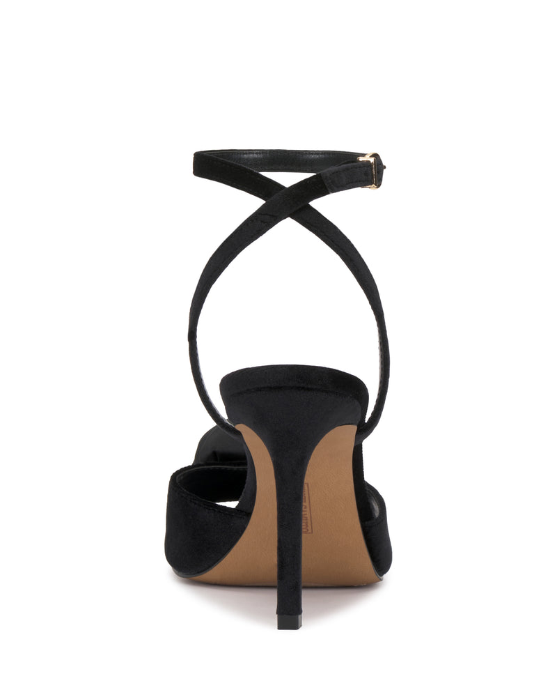 The Aisven Sandal by Vince Camuto is a black high-heeled sandal shown from the back, featuring a slender stiletto heel and black ankle straps that crisscross above the heel and fasten with a small buckle. The sole is tan colored.