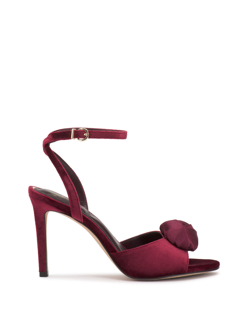 The Vince Camuto Aisven Sandal in burgundy features a high heel, ankle strap, open toe, and a decorative flower—perfect for evening events.