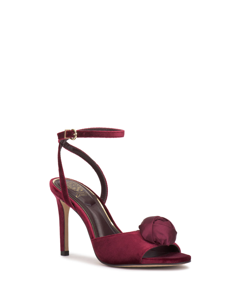 The Vince Camuto Aisven Sandal is a burgundy high-heeled sandal with an ankle strap and large fabric rose detail, featuring a slim heel ideal for elegant evening events.