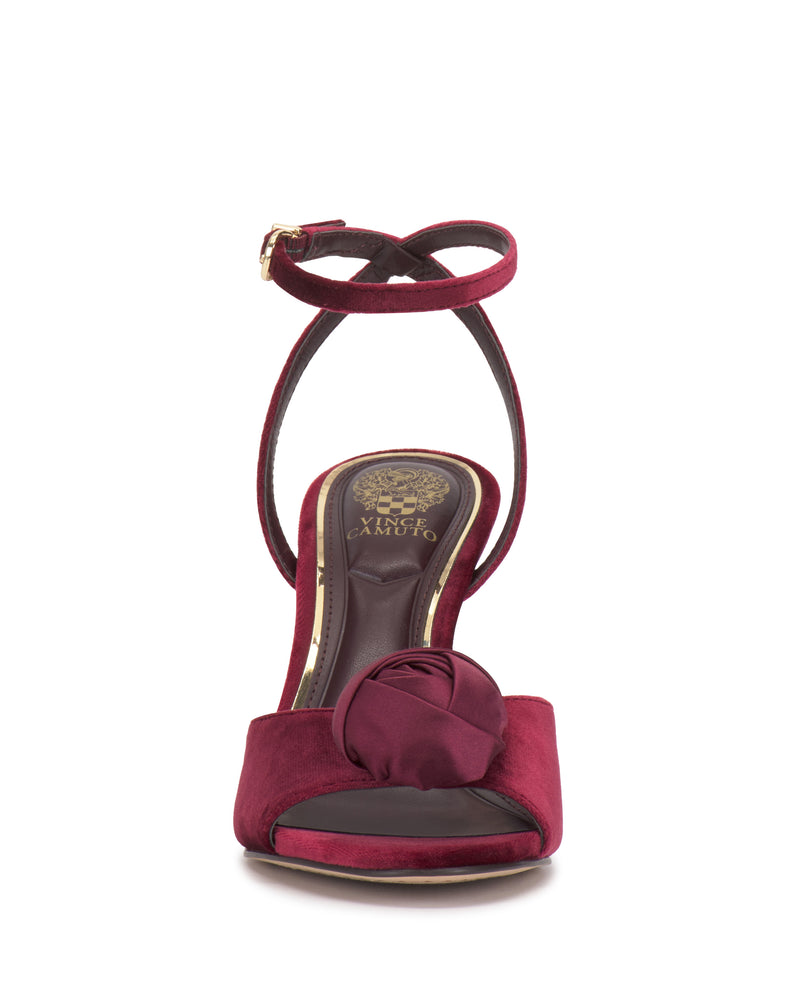 Front view of the Vince Camuto Aisven Sandal in burgundy with a high heel, ankle strap, and fabric rose—perfect for evening events. Gold lettering and a floral emblem accent the insole.