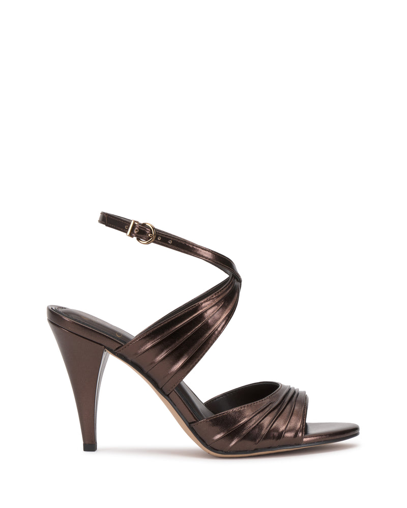 The Vince Camuto Altnori Sandal is a metallic bronze heeled sandal with an ankle strap and buckle, crisscross bands, and a rounded open toe, shown on a white background.