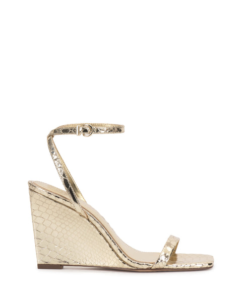 The Ambee Wedge Sandal by Vince Camuto features a gold metallic snakeskin texture, square toe, slim toe strap, and buckle ankle strap. With a moderate wedge heel and minimalist design, it's ideal for formal occasions.