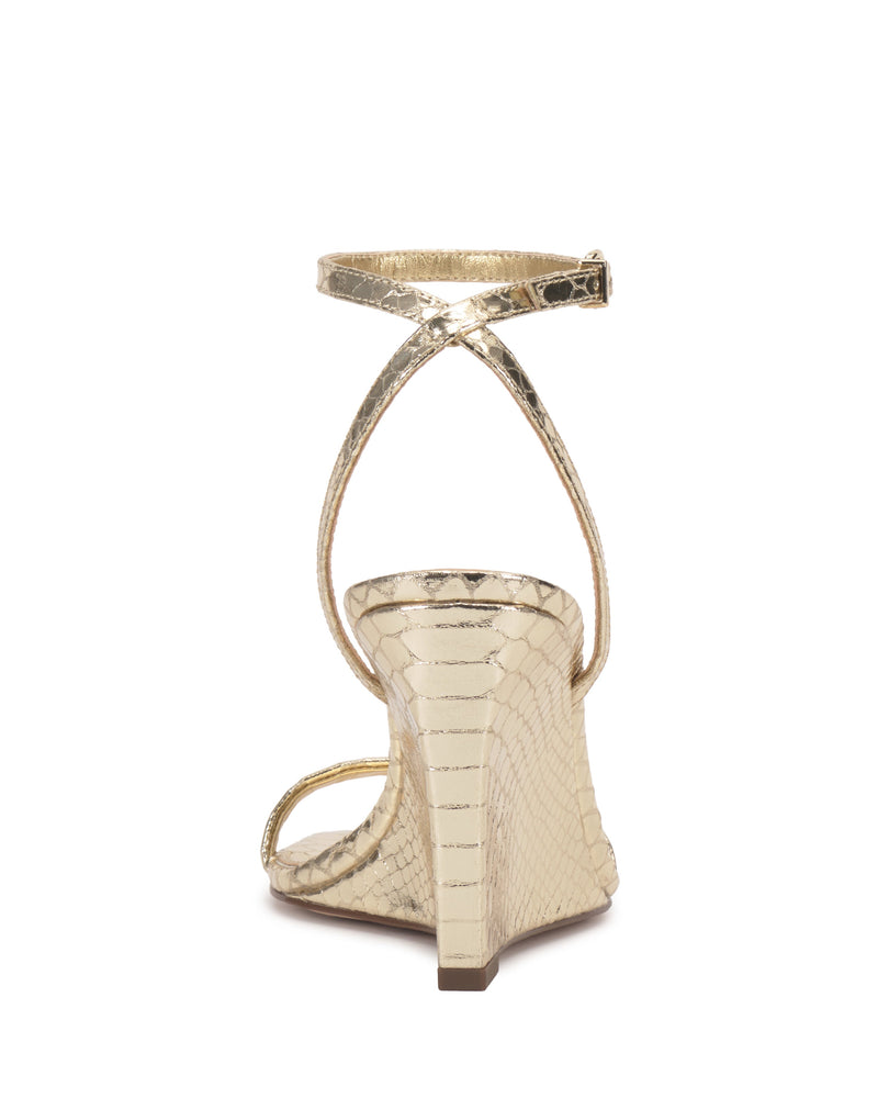 The Ambee Wedge Sandal by Vince Camuto features a gold, snakeskin-textured finish, closed back, slim buckled ankle strap, and open square toe—ideal for formal occasions. Shown here from the rear view.