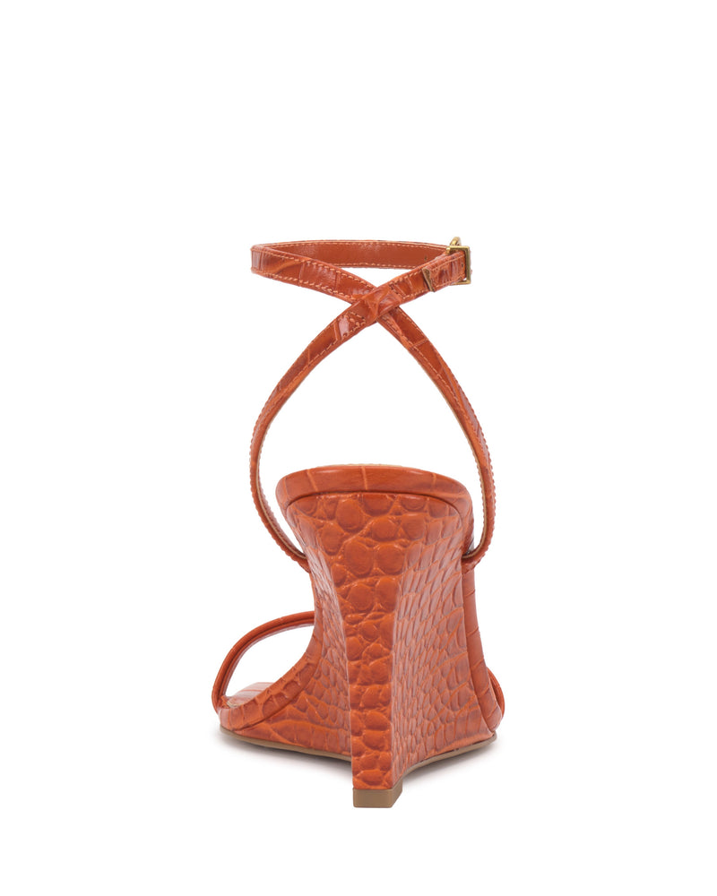 The Vince Camuto Ambee Wedge Sandal features an orange, crocodile-patterned design with a high wedge heel, square toe, and crisscross ankle straps—offering chic style ideal for formal occasions.
