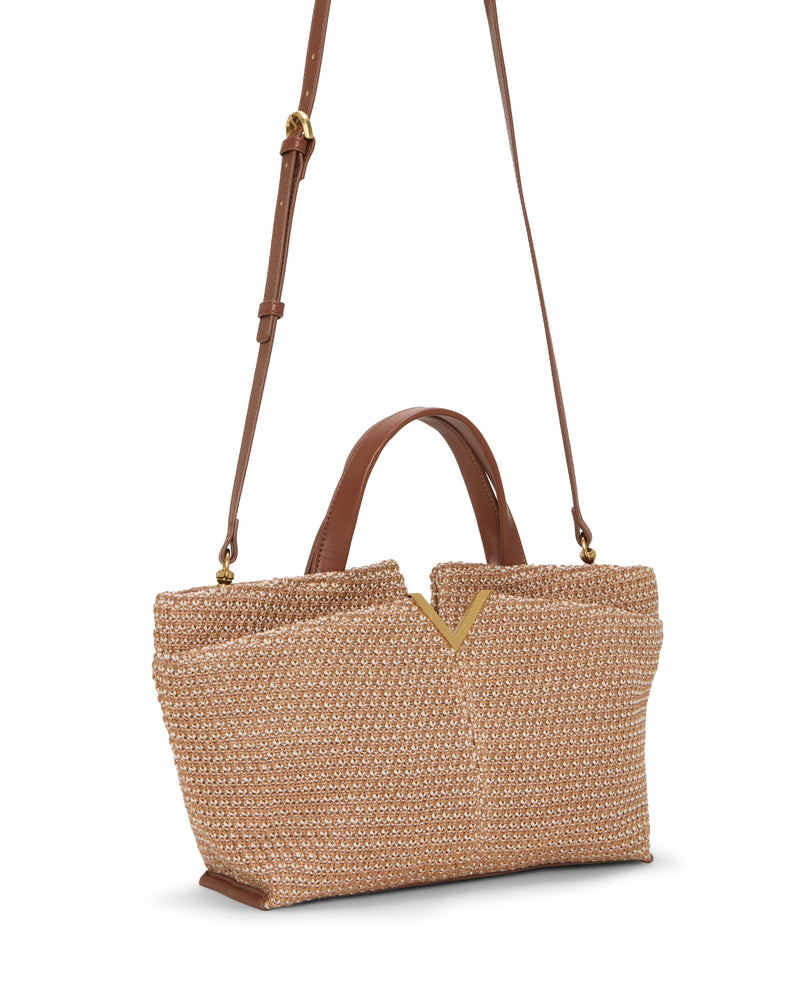 The Vince Camuto April Satchel Bag features a woven straw design, brown leather handles, and a long adjustable shoulder strap. A V-shaped notch accents the opening. Shown against a white background.
