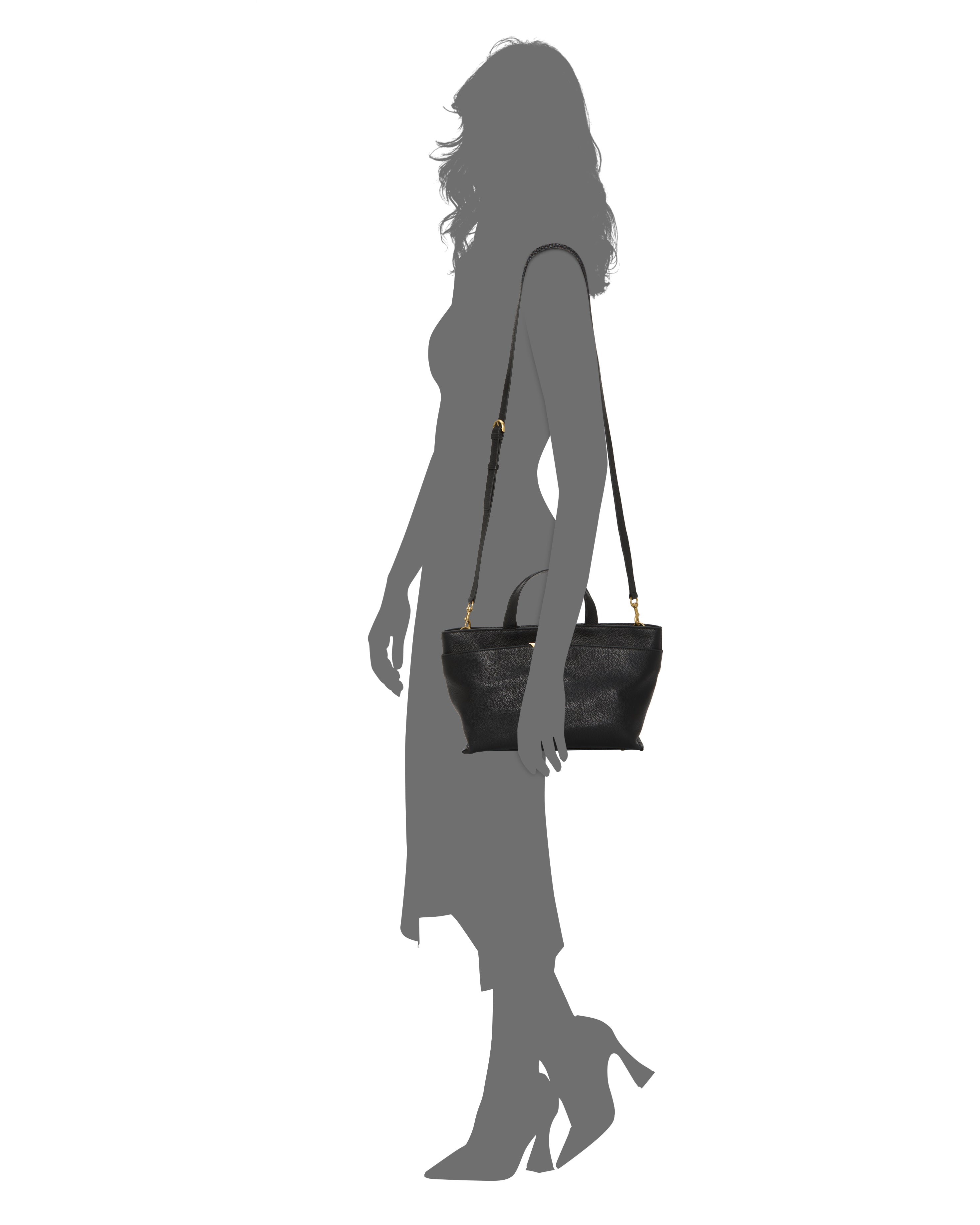 The Vince Camuto April Satchel Bag, featuring black leather and gold hardware, is shown hanging from the shoulder of a silhouetted woman in a long dress and heels, posed in profile against a white background.