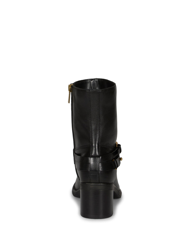 The Vince Camuto Armia Bootie is shown from the back in black leather, highlighting a chic block heel, side zipper, and a decorative buckle harness strap around the ankle. The background is plain white.