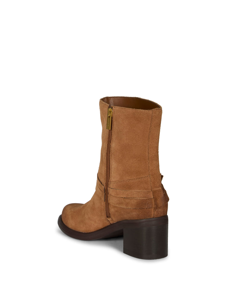 The Vince Camuto Armia Bootie is a brown suede ankle bootie with a chunky block heel and side zipper, shown from a rear three-quarter angle. It features decorative stitching, a harness accent, and a slightly pointed toe.