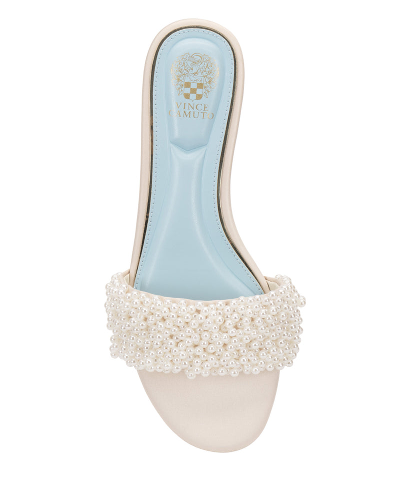The Vince Camuto Balea Beaded Sandal is a stylish flat with a light blue insole, white upper, and wide strap adorned with small white pearls. Gold "Vince Camuto" branding adds elegance, making it perfect for any occasion.