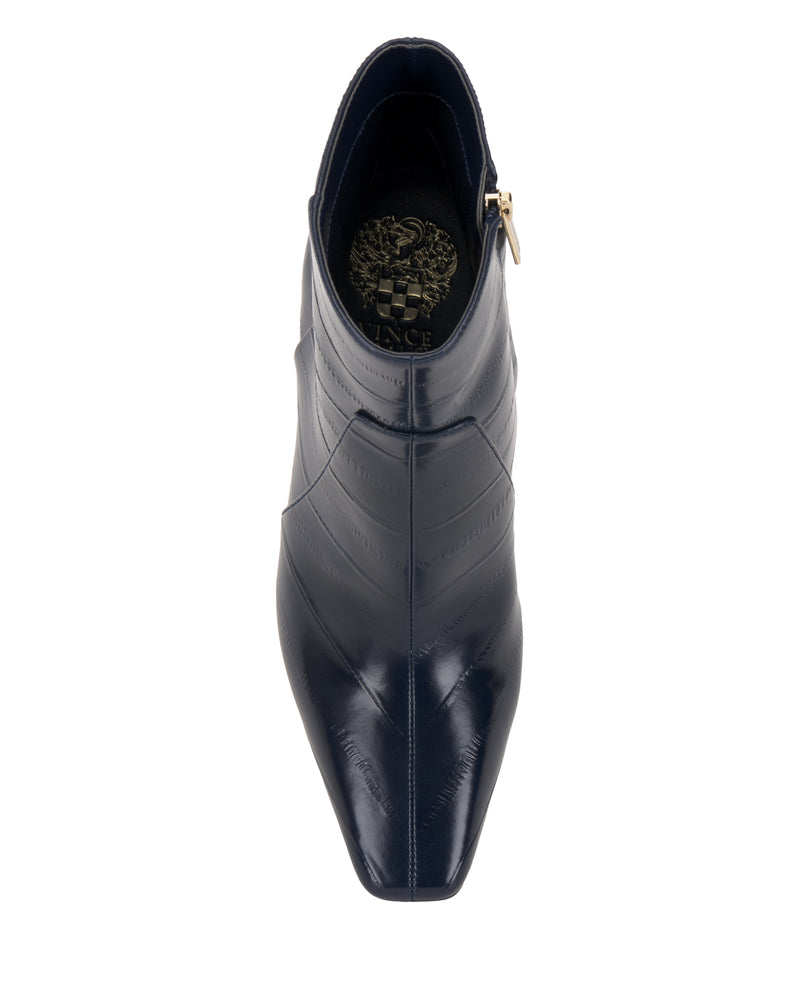 A top view of the Vince Camuto Bayla Bootie in dark navy showcases its pointed toe, stitched detailing, and convenient side zipper for easy styling. The insole is adorned with a gold crest design, all set against a clean white background.