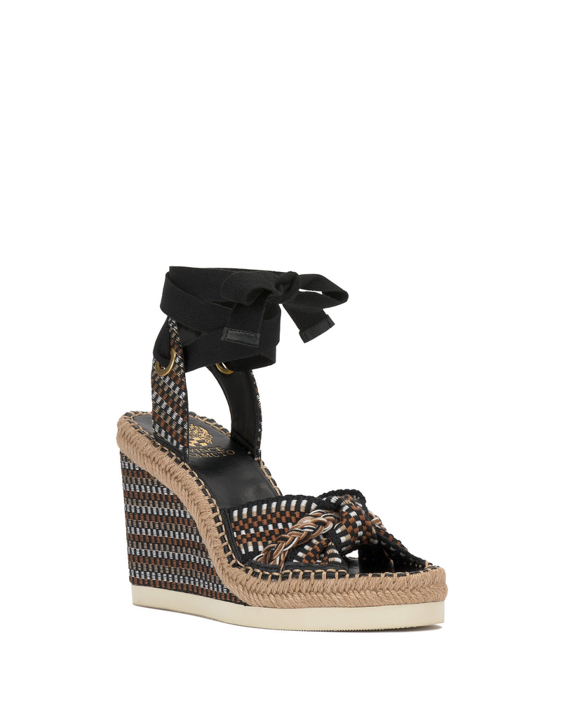 The Vince Camuto Bealie Wedge Sandal features a boho espadrille design with woven platform, braided straps, black ankle ties, layered tan and white sole, and a gold logo footbed for chic, laid-back style.