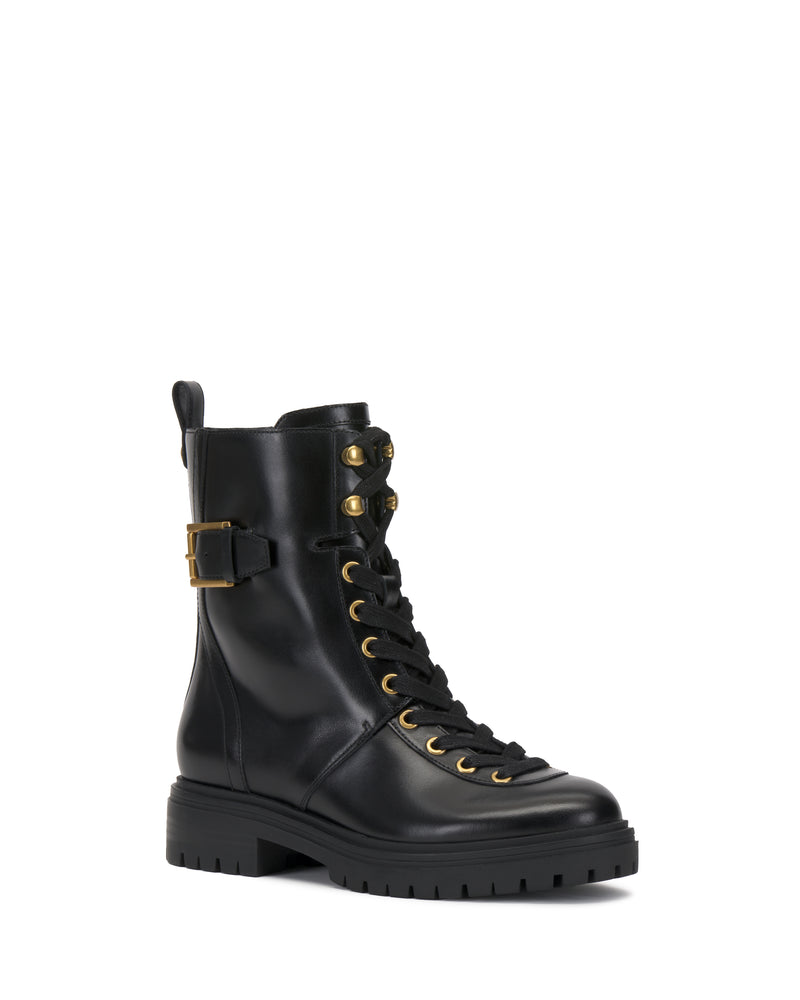 The Becinda Moto Bootie by Vince Camuto is a black leather combat boot featuring gold eyelets, a side buckle, black laces, and a chunky treaded sole.