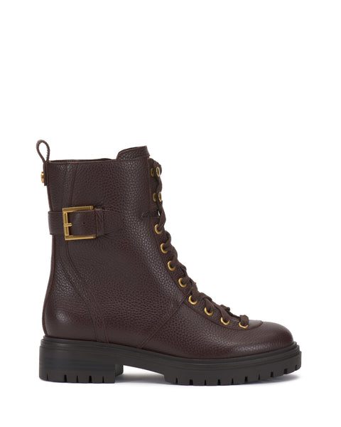 The Vince Camuto Becinda Moto Bootie is a dark brown leather lace-up combat boot featuring gold eyelets, side buckle detail, a pull tab at the back, and a black chunky rubber sole. The boot is displayed from the side against a white background.