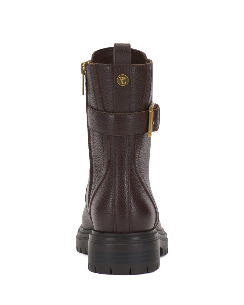 The Vince Camuto Becinda Moto Bootie is a brown leather boot displayed from the back, showcasing a gold buckle on the side, a textured finish, a thick black sole, and a small round gold logo near the top.
