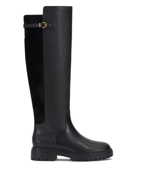 The Bertla Knee High Riding Boot by Vince Camuto features a tall black silhouette with a chunky sole, rounded toe, and a decorative gold buckle on the upper side. Its shaft combines smooth leather with suede-like material for added texture.
