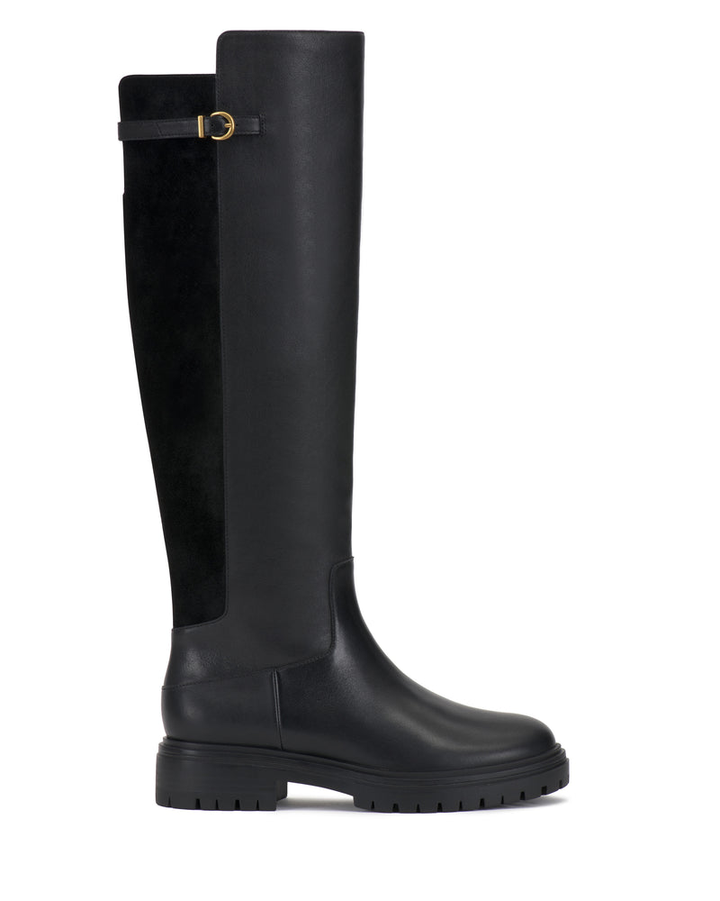 The Bertla Knee High Riding Boot by Vince Camuto features a tall black silhouette with a chunky sole, rounded toe, and a decorative gold buckle on the upper side. Its shaft combines smooth leather with suede-like material for added texture.