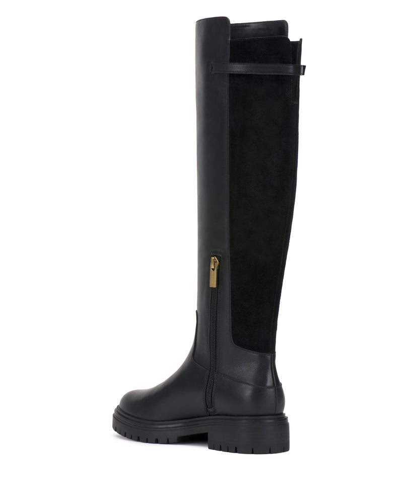 The Bertla Knee High Riding Boot by Vince Camuto is a single black boot featuring a side zipper, low chunky heel, and a combination of smooth leather and suede panels.