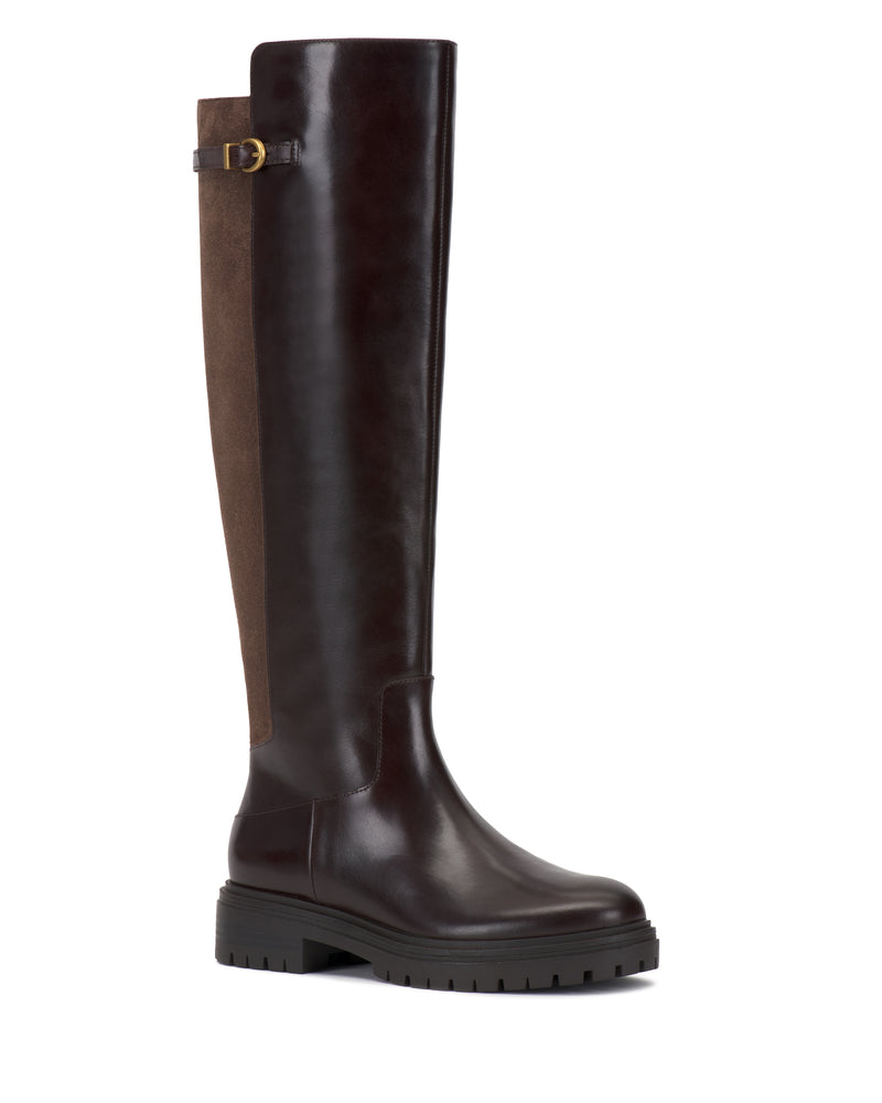 The Bertla Knee High Riding Boot by Vince Camuto features a tall silhouette with a dark brown leather front, a brown suede back panel, side buckle detail, and a chunky black sole.