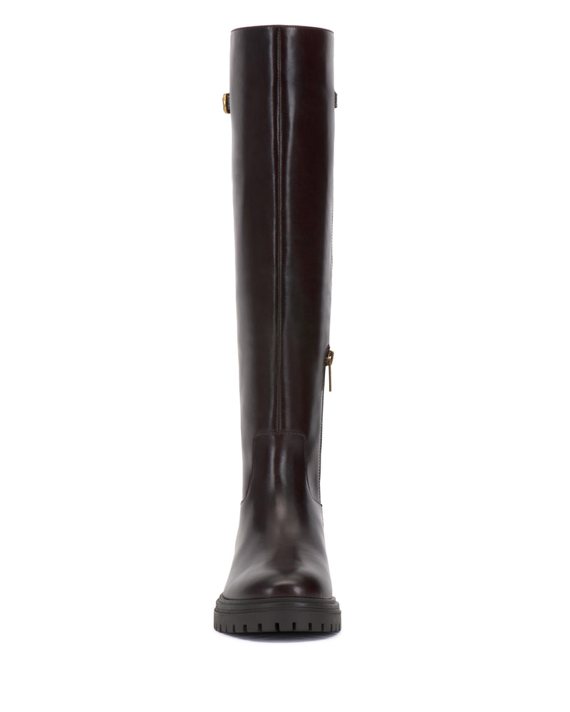 Front view of the Vince Camuto Bertla Knee High Riding Boot, featuring tall, dark brown leather with a side zipper and a decorative buckle near the top. The boot has a round toe and a rugged, textured black sole.