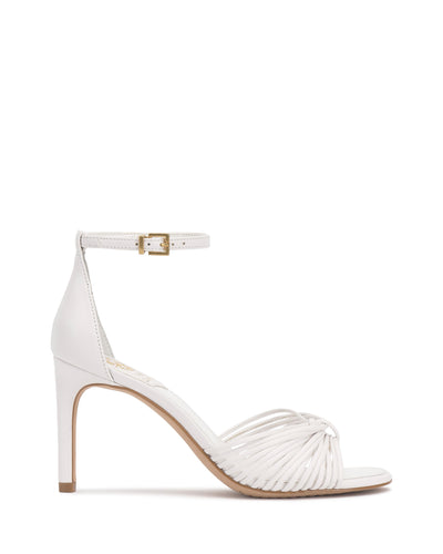 The Blaine Sandal by Vince Camuto features white straps with an ankle strap and gold buckle, open toe, woven front detailing, a slim mid-heel for elegance, and a light tan sole for a chic finish.