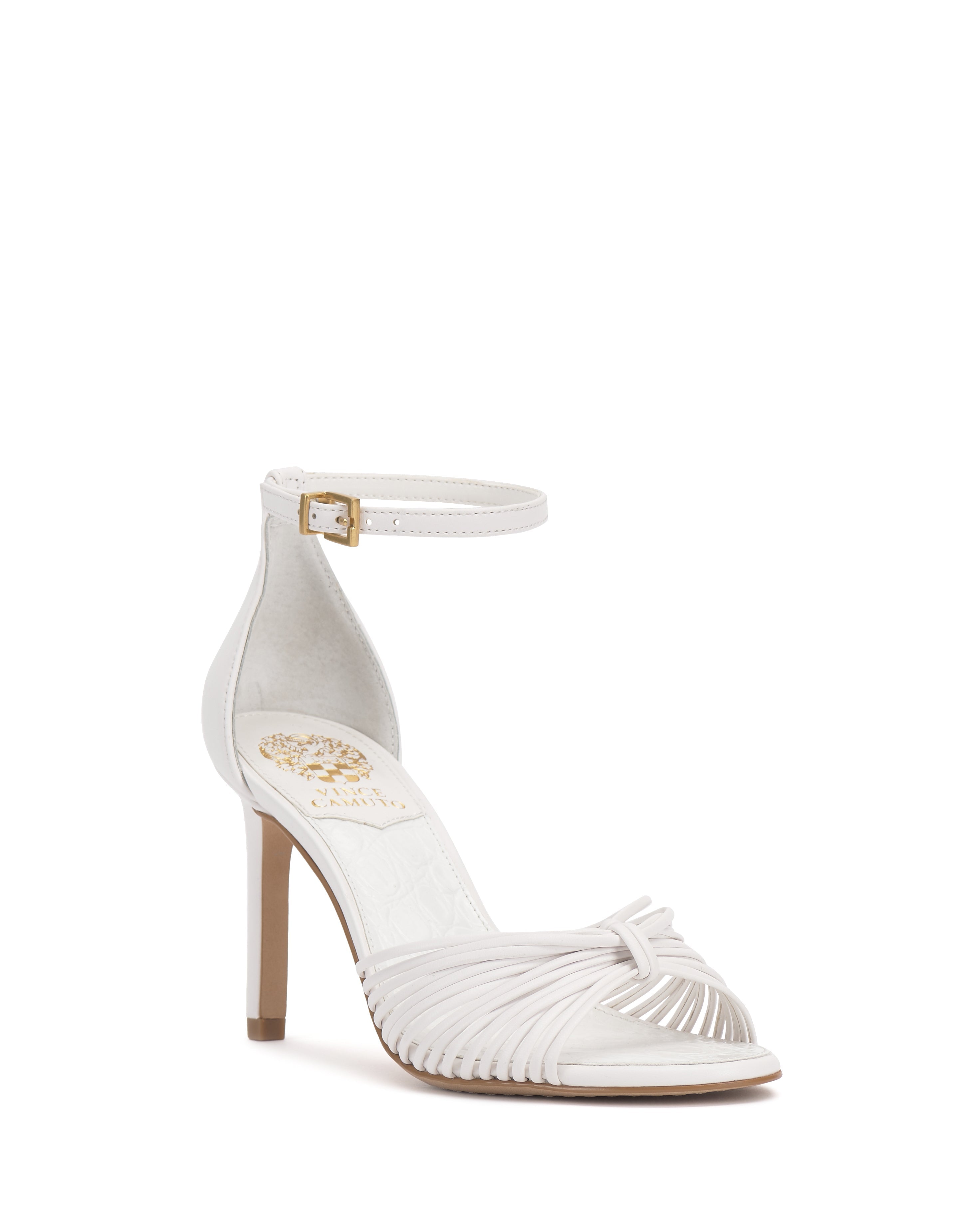 The Blaine Sandal by Vince Camuto features a white strappy design, tall stiletto heel, open toe, ankle strap with gold buckle, and a gold emblem on the insole.