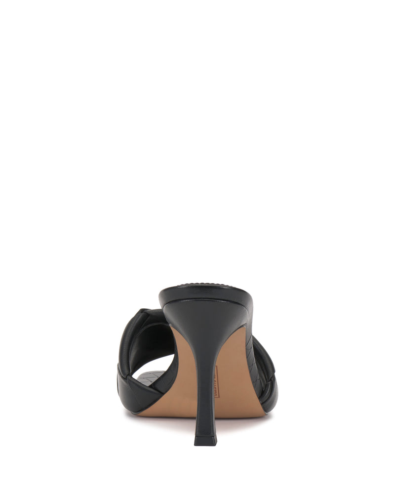 The Vince Camuto Brelanie Woven Mule is a black heeled sandal viewed from the back, highlighting its thin stiletto heel and tan sole against a white background.
