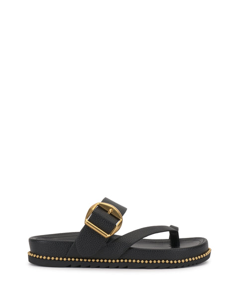 The Camilo Slide by Vince Camuto is a black thong sandal with a wide buckle strap featuring a large gold buckle. Its flat, contoured sole is decorated with small gold studs along the edge for added style and comfort.