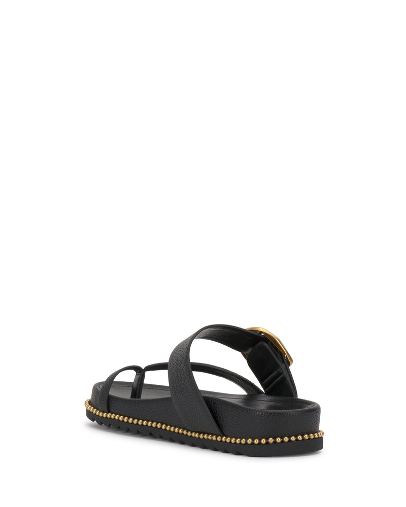The Vince Camuto Camilo Slide is a black sandal with crisscross buckle straps, a gold buckle, contoured footbed, flat sole, and small gold studs along the edge, shown angled on a white background.