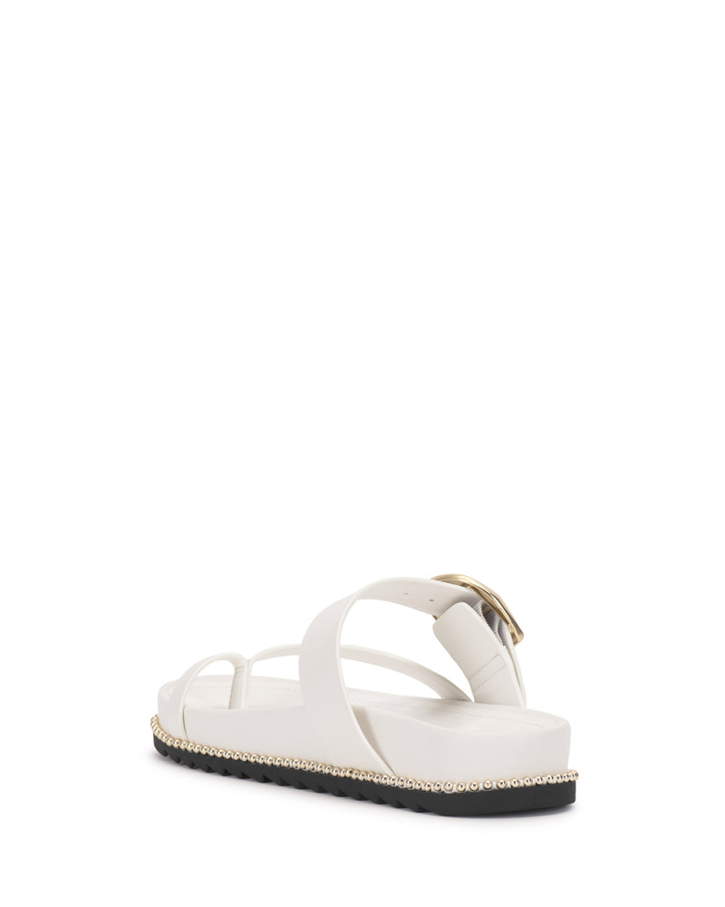 The Vince Camuto Camilo Slide is a white sandal with crisscross buckle straps, a contoured footbed, and pearl-like beads around the sole, shown from a rear side angle against a white background.