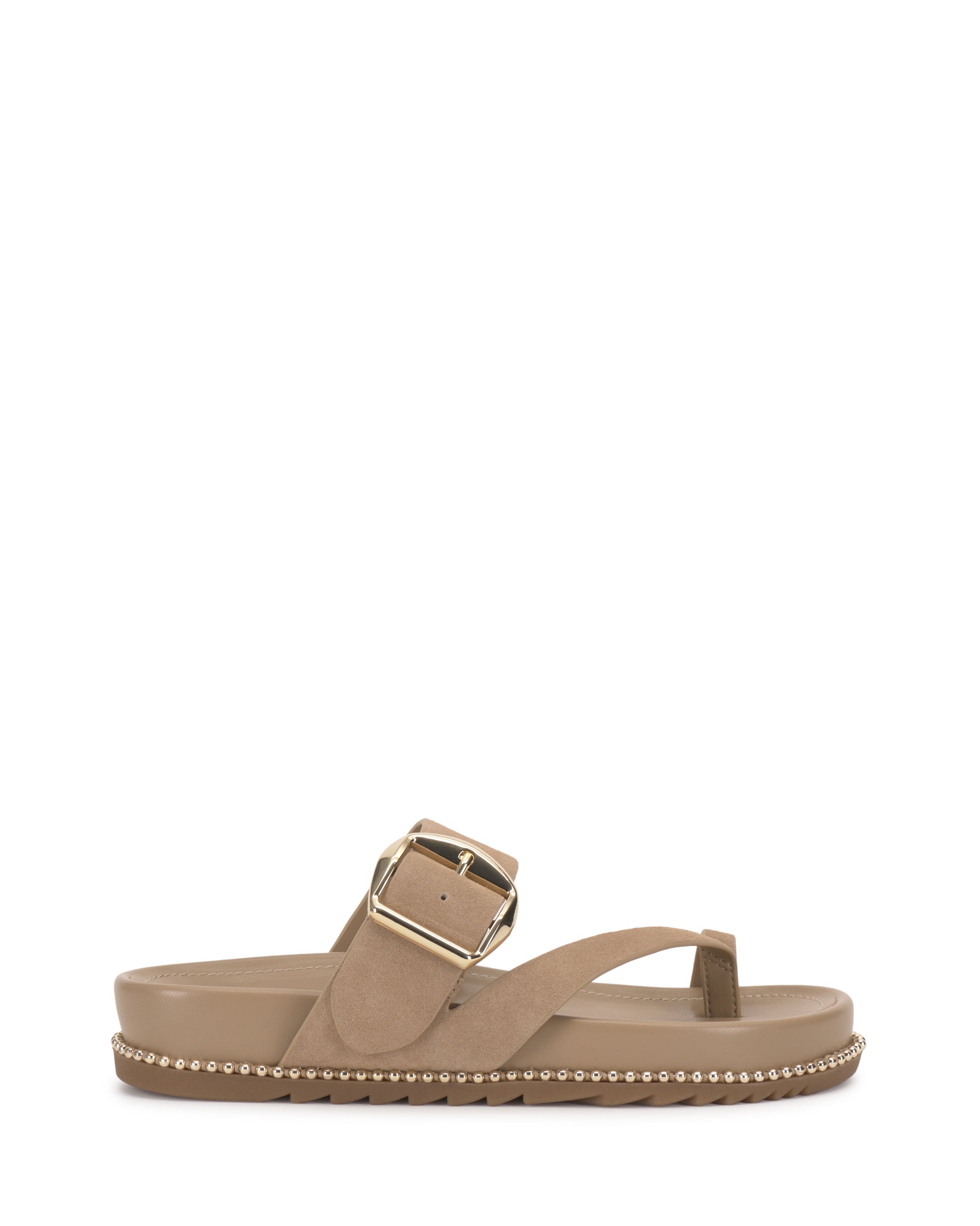 The Camilo Slide by Vince Camuto is a tan sandal with a wide suede buckle strap, large gold buckle, toe divider, flat sole, and metallic stud accents along the edge.