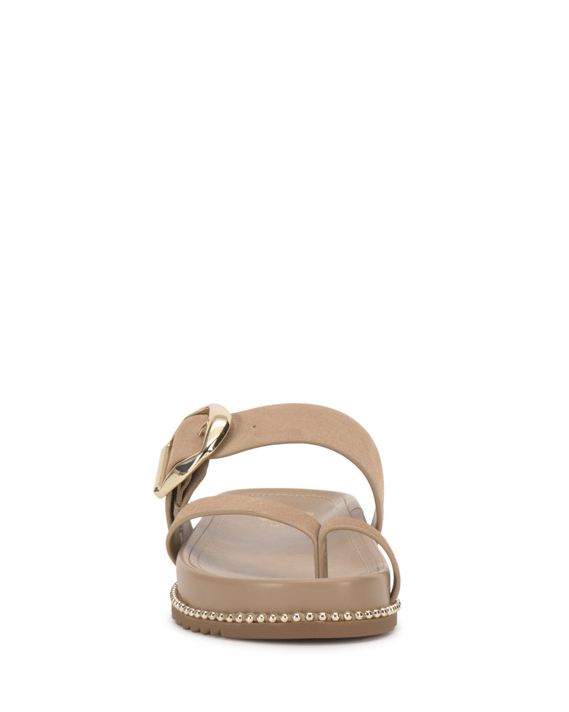 The Vince Camuto Camilo Slide features a beige design with a side buckle strap, large gold buckle, decorative studs along the edge, a clear contoured footbed, and an open toe.