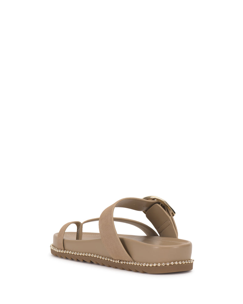 The Vince Camuto Camilo Slide is a tan sandal featuring a thick crisscross buckle strap, ankle strap with buckle, and low platform sole accented with metallic studs. Seen from the back, it offers a contoured footbed for comfort.