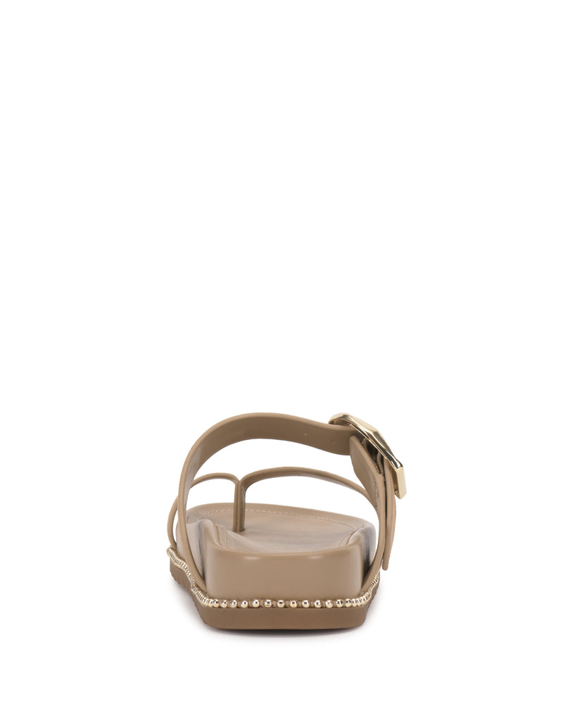 The Vince Camuto Camilo Slide is a tan flat sandal seen from the back, featuring an ankle gold buckle strap and metallic studs along the sole for a chic, detailed finish.