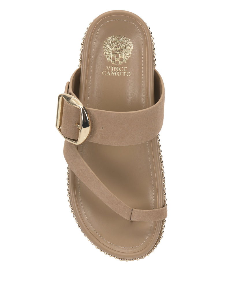 The Vince Camuto Camilo Slide features a tan wide band with a large gold buckle, toe loop, studded trim, and contoured footbed embossed with the Vince Camuto logo in gold. The sandal is shown from an overhead view.